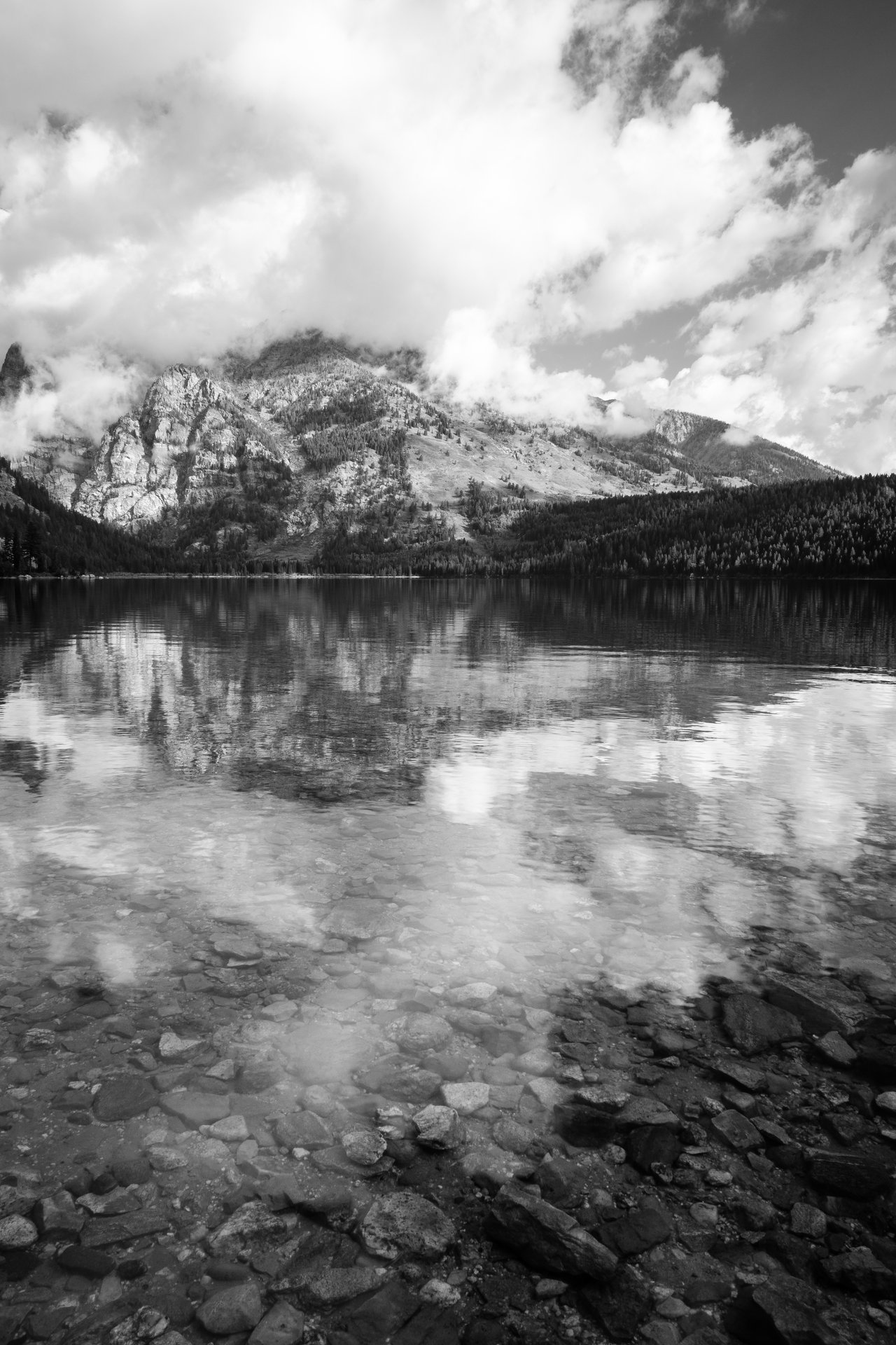 Rocks under the surface of Phelps Lake, with Albright Peak shrouded in clouds in the distance.