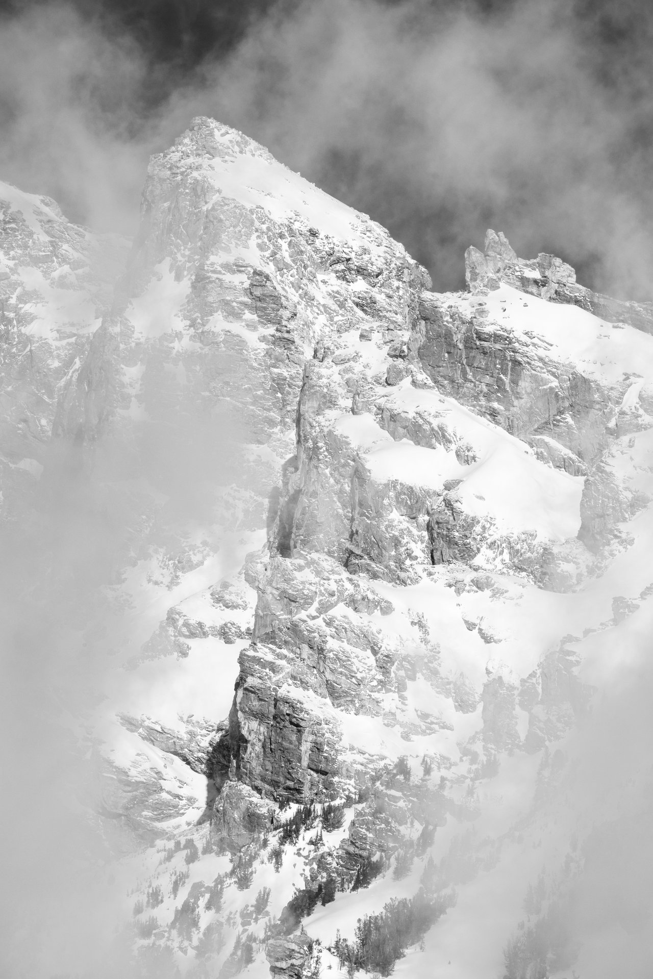 A close-up of one of the peaks of the Teton range, surrounded by clouds.