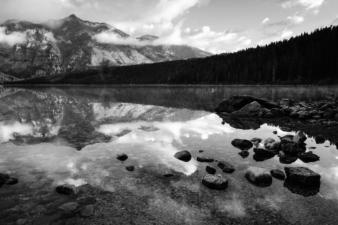 Rocks near the shore of Phelps Lake, with Albright Peak reflected in the water.