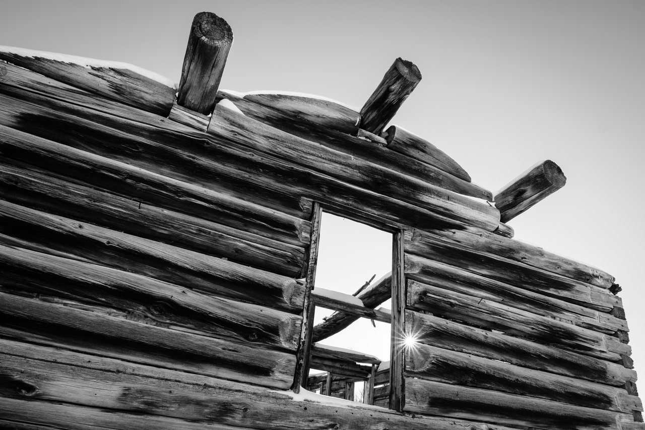 The facade and window of the Shane Cabin at Grand Teton National Park, with the sun shining between the logs.