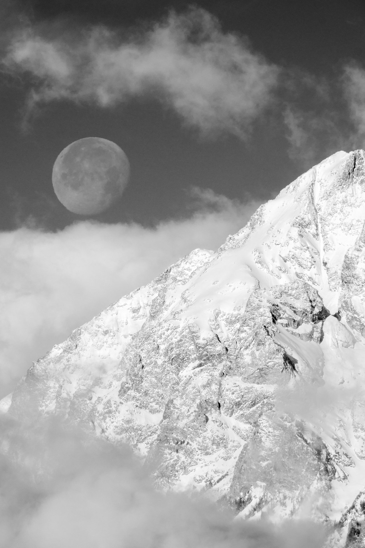 A snow-covered mountain peak rises above clouds in the foreground, with the moon visible in the sky amidst scattered clouds.